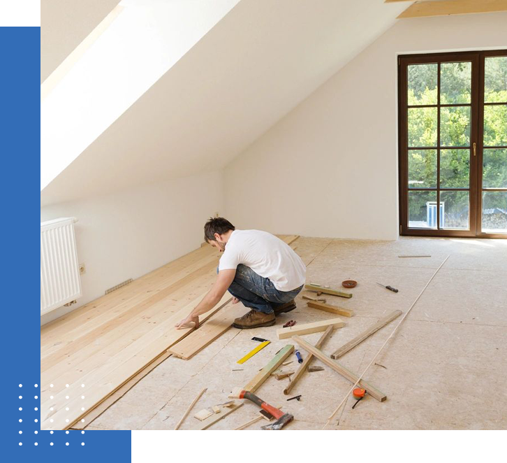 A man laying down wood in an unfinished room.