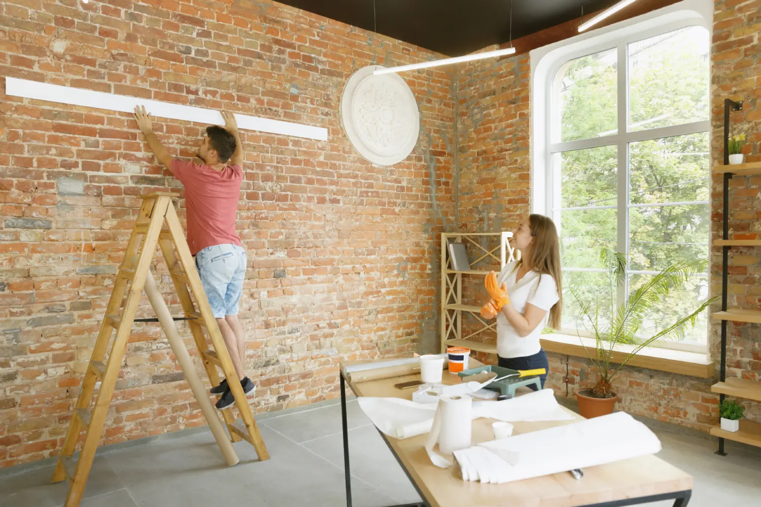 A man and woman are painting the wall of their home.